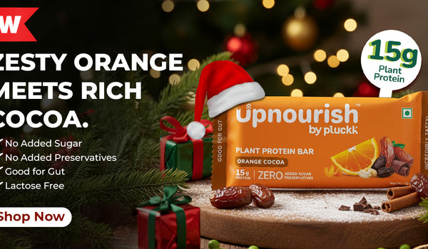 Upnourish plant protein bar with Christmas decorations in the background. A banner representing wintr and christmas vides in the background while text read new zesty orange meets rich cocoa no added sugar no added preservative good for gut lactose free shop now 15g protein Upnourish, plant protein bar, plant protein bar india, orange protein bar, ornage coco plant protein bar, 15 gram, offer 20% off,  coupen code 